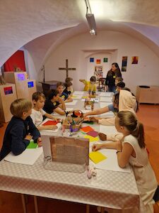In einem farbenfrohen, gewölbten Raum sitzen Kinder um einen Tisch und basteln.
